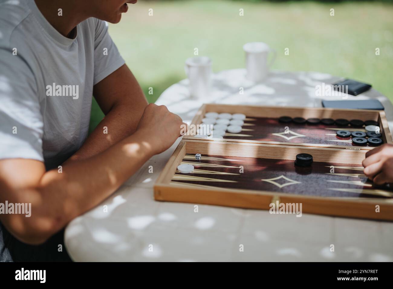 Due amici si divertono a giocare a backgammon all'aperto in una giornata di sole con tazze da caffè sullo sfondo. Foto Stock