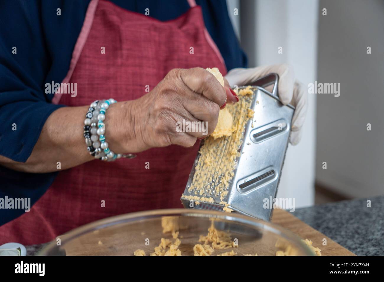 Primo piano delle mani di una donna adulta che grattugia la banana verde su una grattugia per una ricetta dell'America Latina proveniente dall'Ecuador, dalla Colombia o dall'America centrale Foto Stock