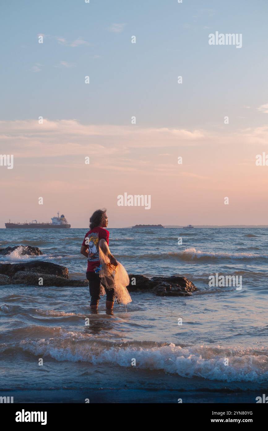 Un pescatore si prepara e aspetta il momento giusto per gettare la rete sulla spiaggia di Balikpapan, Kalimantan orientale, Indonesia Foto Stock