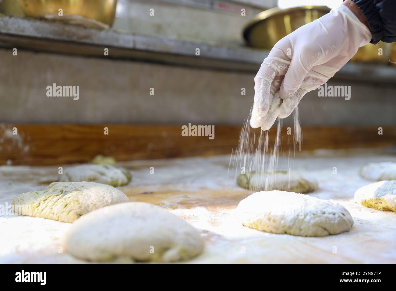 Il personale ha cosparso la farina sull'impasto.Xining, Cina.20 novembre 2024. Il processo di produzione del Kunguo Momo prevede che il personale versi olio di colza nell'impasto fermentato, aggiunga spezie naturali come lievito rosso, curcuma e farina di soia, e poi le distribuisca uniformemente a mano per formare l'impasto. Il nome "Kunguo" deriva dagli esclusivi stampi metallici utilizzati nel processo di produzione. È stato riferito che attraverso piattaforme di live streaming online, oltre ad essere venduto a varie parti della Cina, Kunguo Momo di Haiya Kunguo Momo Industry base è stato esportato in paesi come Singapore Foto Stock