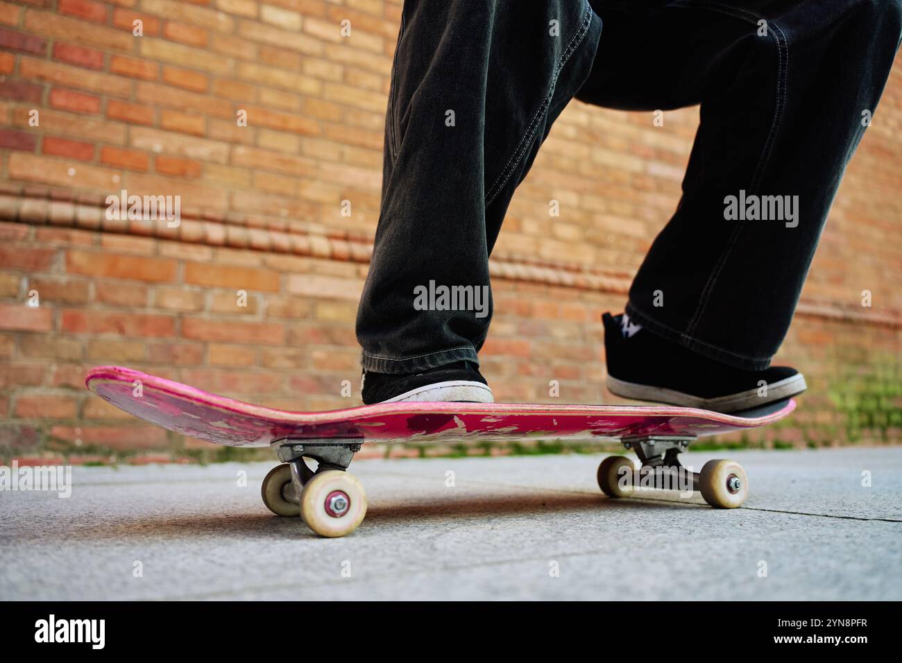 Skateboarder che fa il trick in Urban Street. Primo piano dello skater che indossa jeans larghi in equilibrio sullo skateboard. Concetto di sottocultura giovanile Foto Stock