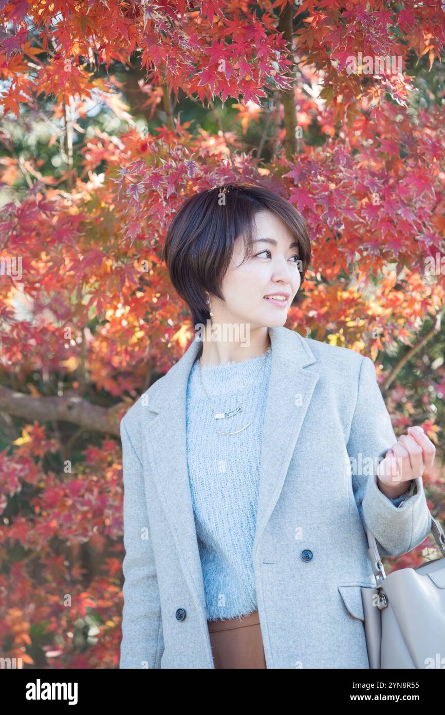 Donna sorridente a 30 anni con foglie autunnali sullo sfondo. Foto Stock