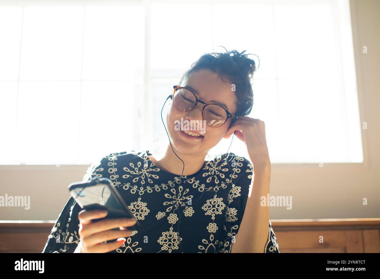 Donna sui vent'anni seduta vicino alla finestra a guardare il suo telefono Foto Stock