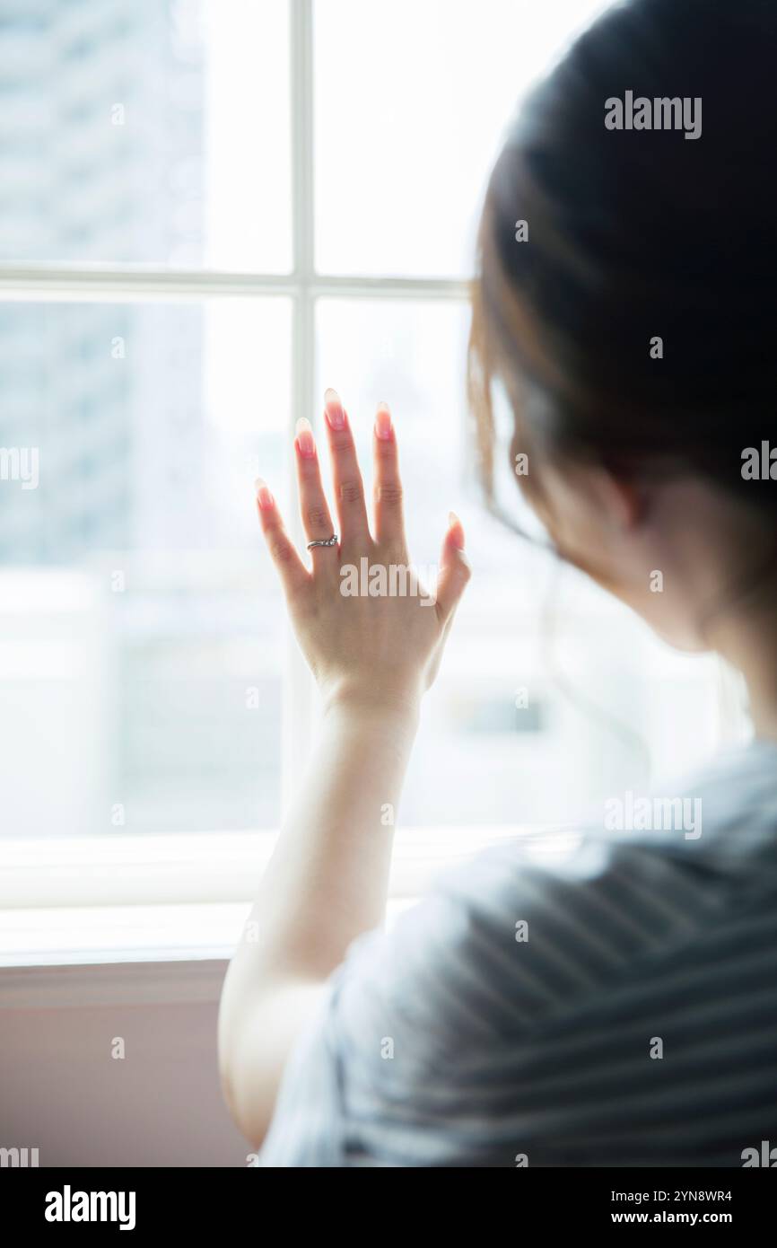 Donna dietro la finestra che guarda l'anello al dito dell'anello Foto Stock