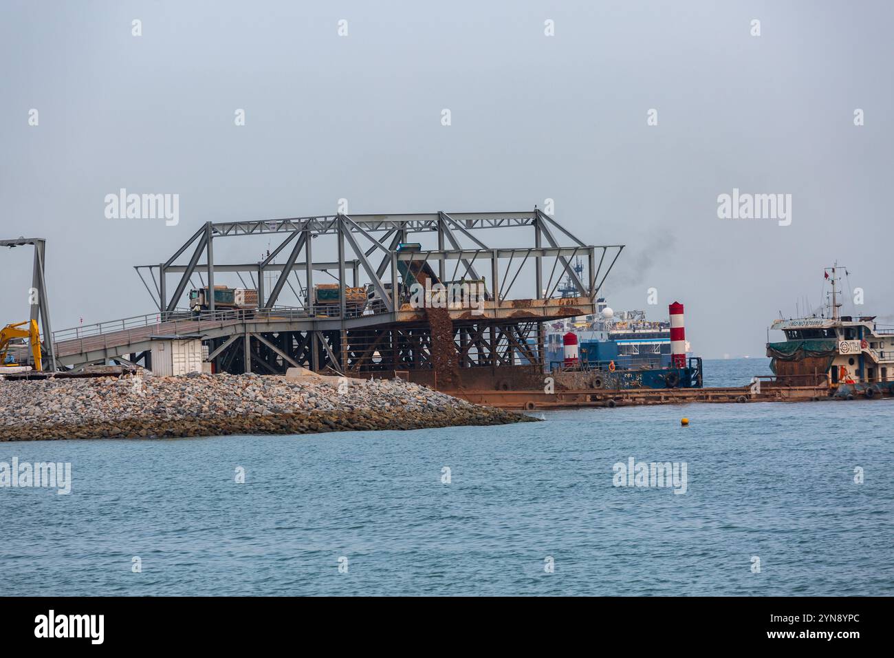 Il camion della sabbia versa la sabbia in mare per lavori di bonifica del terreno. Lavori industriali di riempimento del terreno a Marina Bay. Singapore Foto Stock