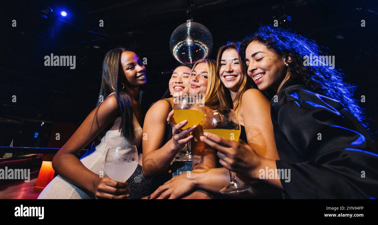 Gruppo di amici che si godono un drink in un vivace nightclub. Risate e gioia riempiono la scena mentre festeggiano insieme sotto le luci della discoteca. Foto Stock