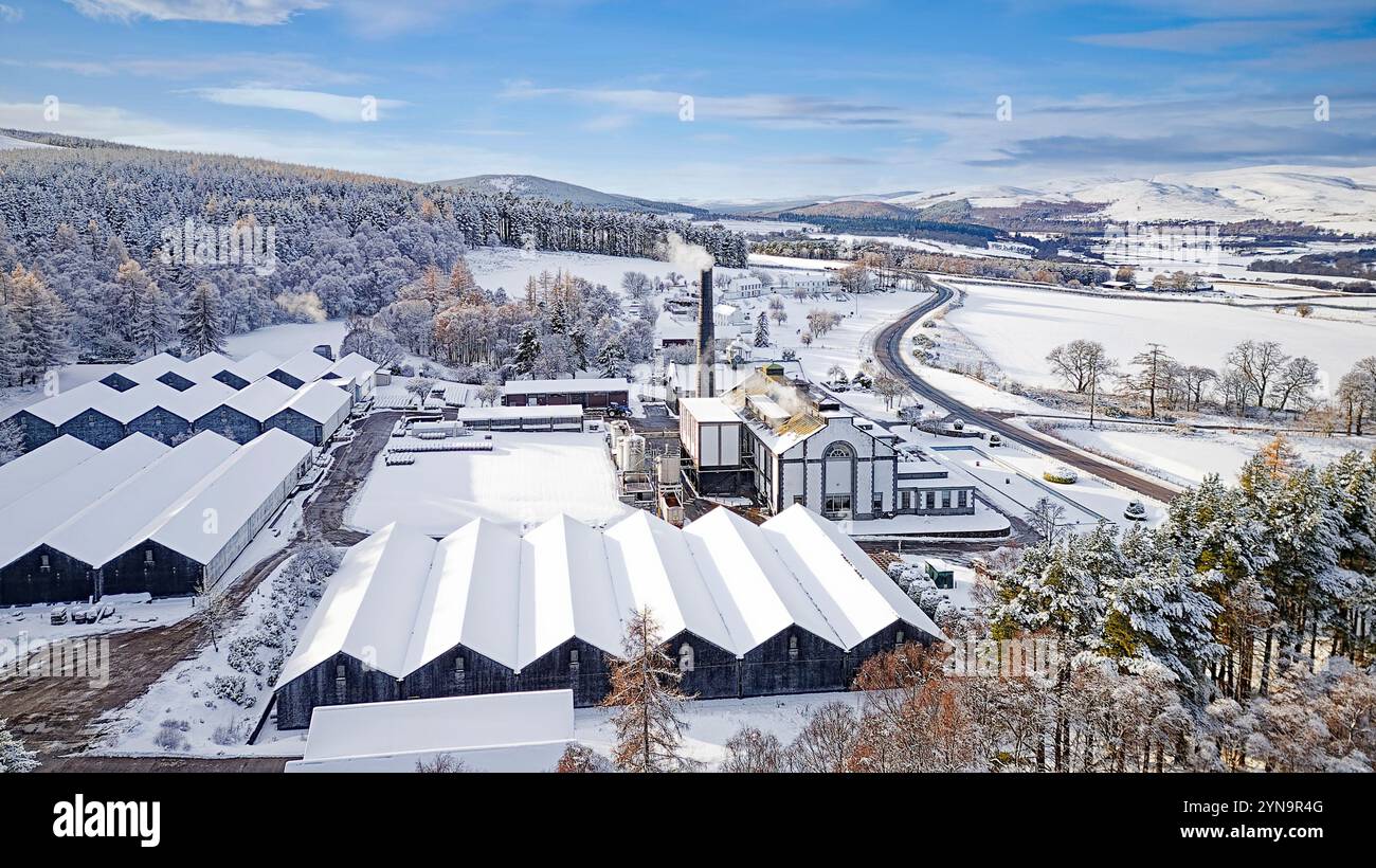 Tormore Distillery una distilleria di whisky Scotch al malto di Speyside con un cielo blu e neve incontaminata sopra edifici storici, colline e abeti Foto Stock