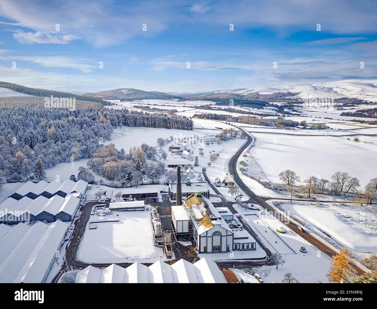 Distilleria Tormore distilleria di whisky Scotch al malto Speyside con cielo blu e neve sopra edifici storici, colline e abeti Foto Stock