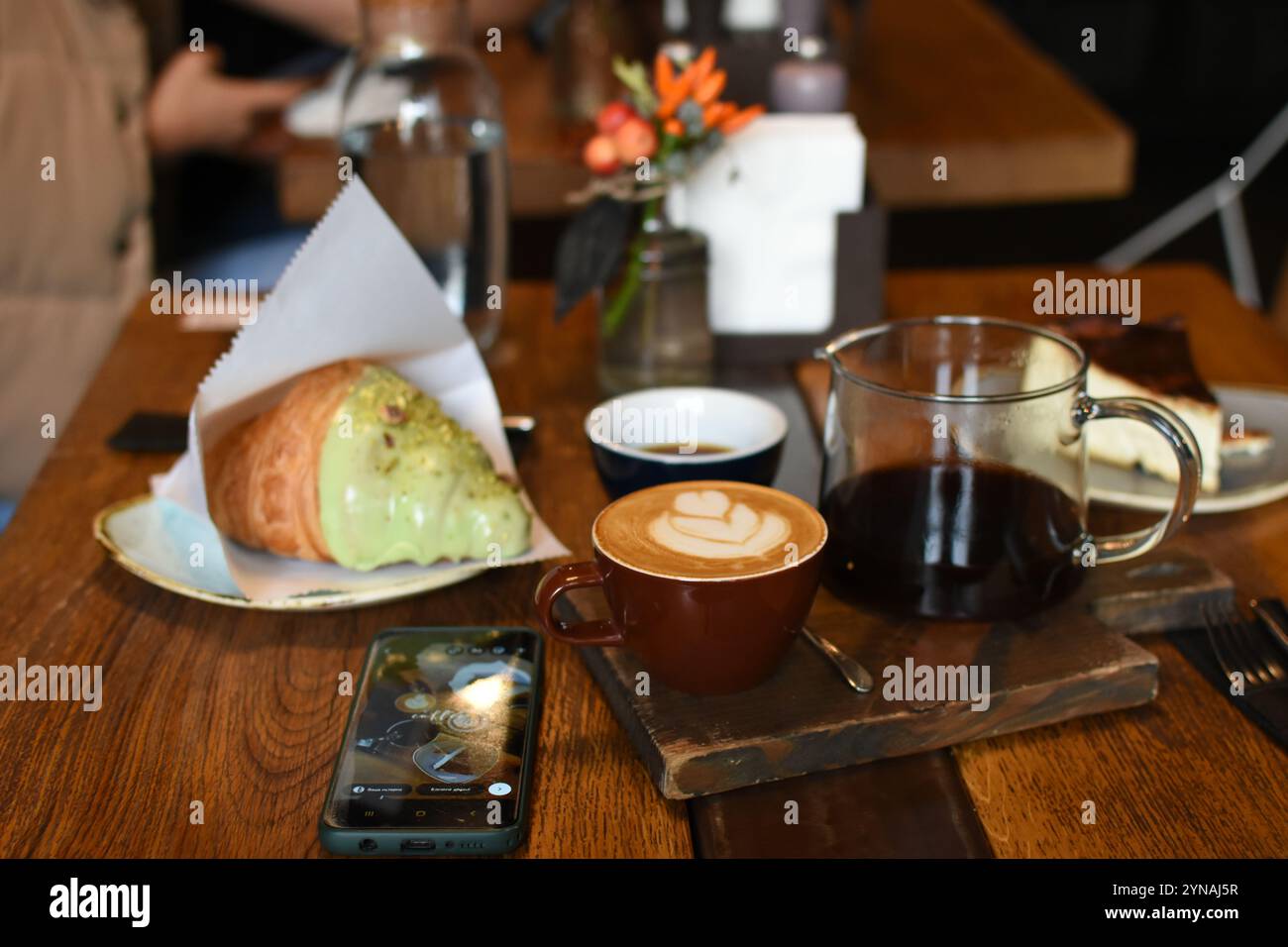 Un delizioso ambiente da caffe' caratterizzato da un latte con arte, una teiera di caffe', un croissant burroso e una cheesecake. Perfettamente accogliente Foto Stock