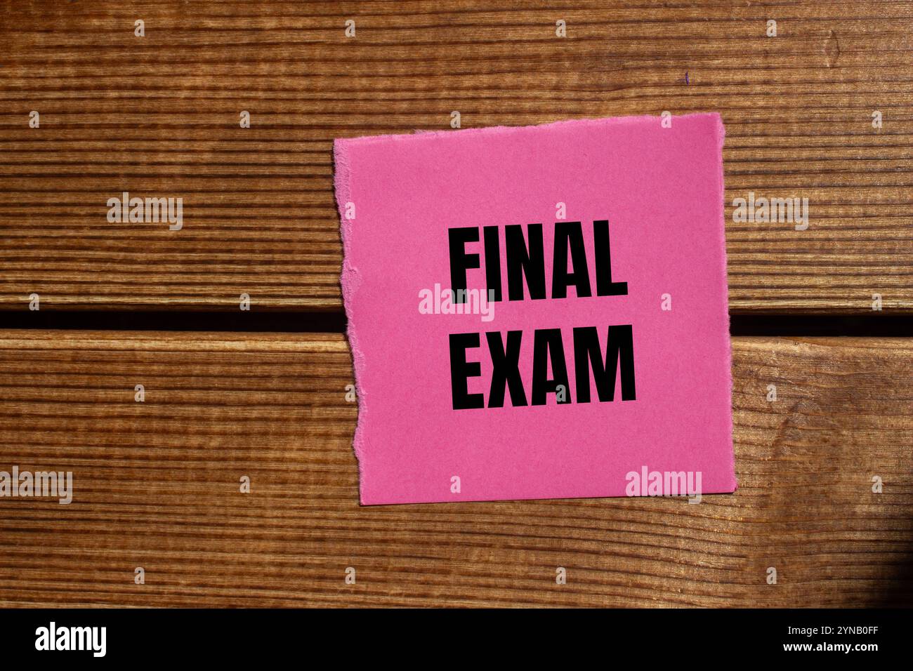 Messaggio finale dell'esame scritto su un pezzo di carta rosa strappato con sfondo in legno. Simbolo dell'esame finale concettuale. Copia spazio. Foto Stock