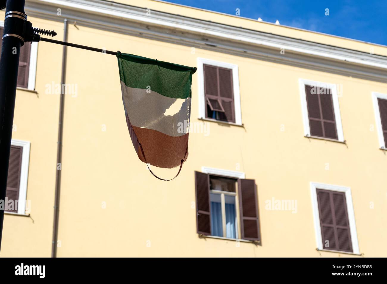 Una bandiera italiana lacerata e infranta sullo sfondo di un edificio giallo a Civitavecchia, in Italia Foto Stock
