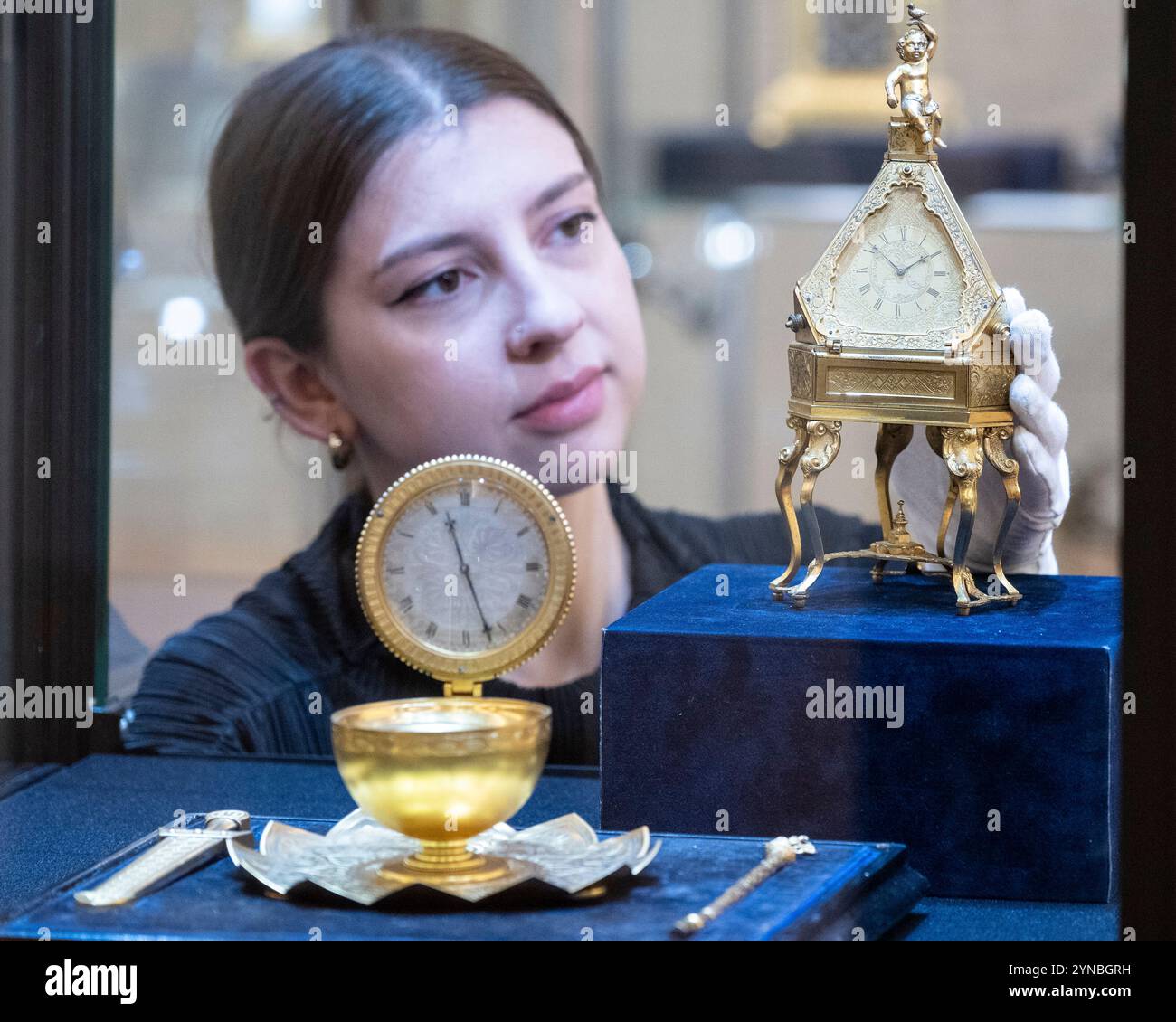 Londra, Regno Unito. 25 novembre 2024. Un membro dello staff con Un elegante e raro compendio di orologio da scrivania in ottone dorato della metà del XIX secolo con calendario e termometro di Thomas Cole, Londra, (stimate £ 15.000 - £ 20.000) in anteprima delle opere nelle aste della stagione invernale dei classici a Bonhams New Bond Street. I lotti saranno messi in vendita con la vendita di orologi di precisione, il 27 novembre, nelle gallerie New Bond Street di Bonhams. Crediti: Stephen Chung / Alamy Live News Foto Stock