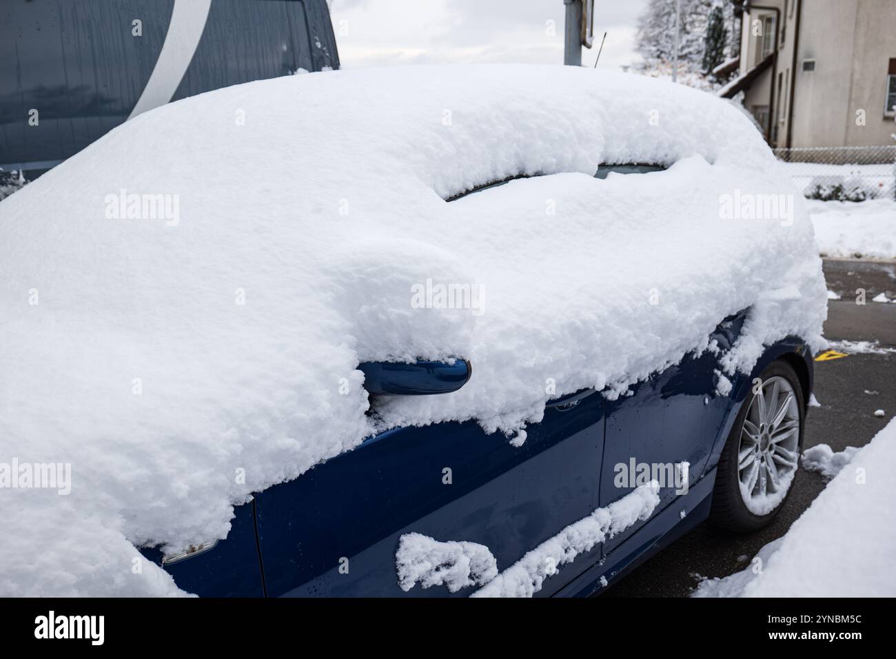 Una piccola auto berlina blu con copertura di neve parcheggiata in strada dopo una forte nevicata. Vista grandangolare ravvicinata, nessuna persona. Foto Stock