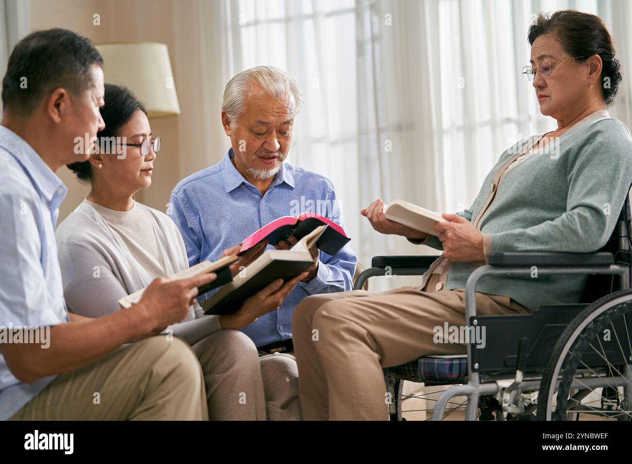 gruppo di anziani asiatici seduti sul divano a casa a leggere la bibbia insieme Foto Stock