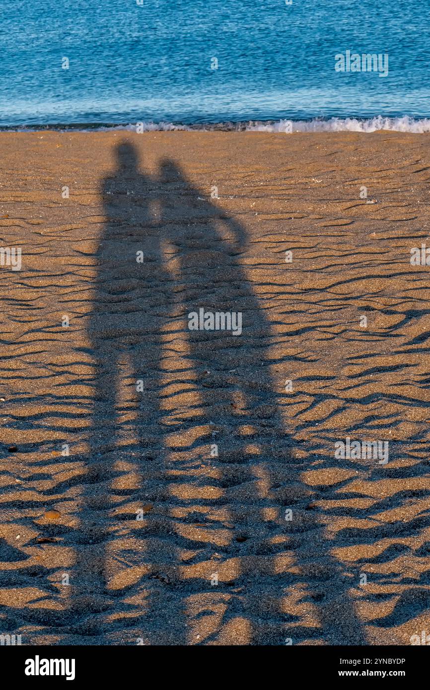 Le lunghe ombre di una coppia su una spiaggia sabbiosa al tramonto con il mare sullo sfondo Foto Stock