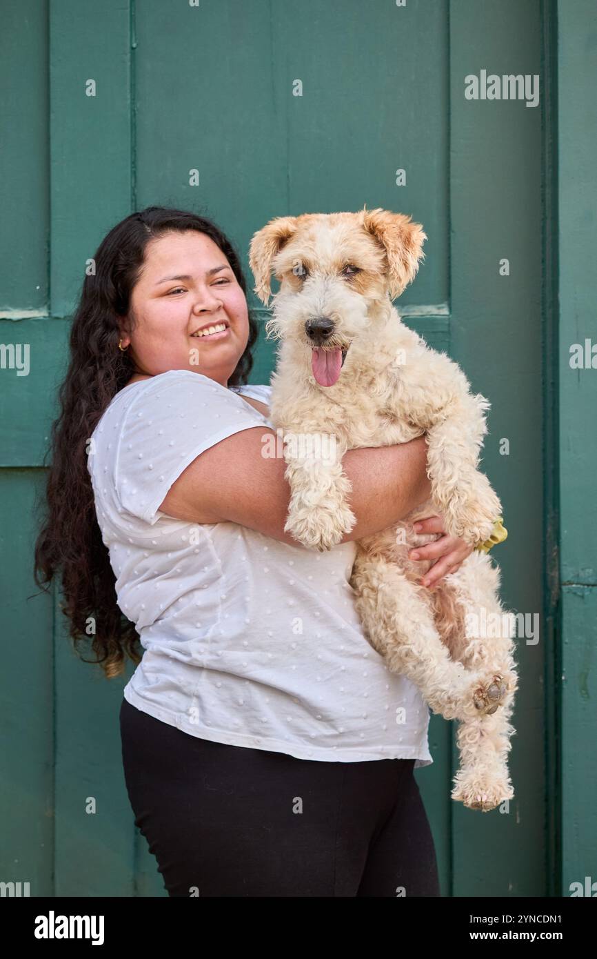 Ragazza latina con in mano un cane Fox terrier. La donna sorride la persona indossa una t-shirt bianca con punti e pantaloni scuri. Il cane, con il Foto Stock