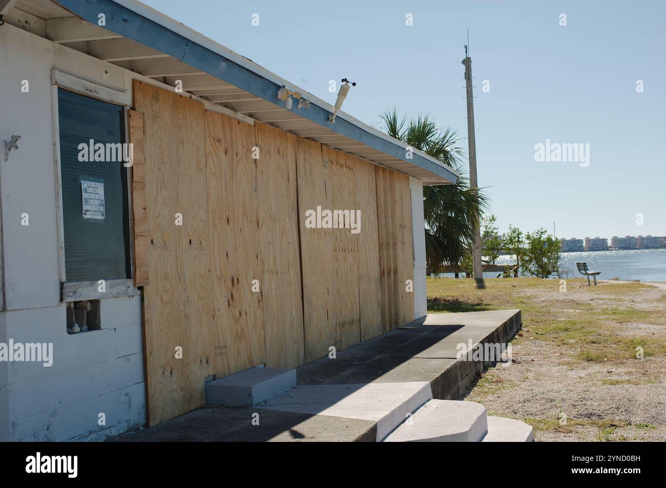 Vecchio edificio con finestre di copertura in compensato sul marciapiede sinistro che conduce le linee del muro del mare fuori dal porticciolo di Gulfport Florida alla Baia di Boca Ciega su un soleggiato Foto Stock