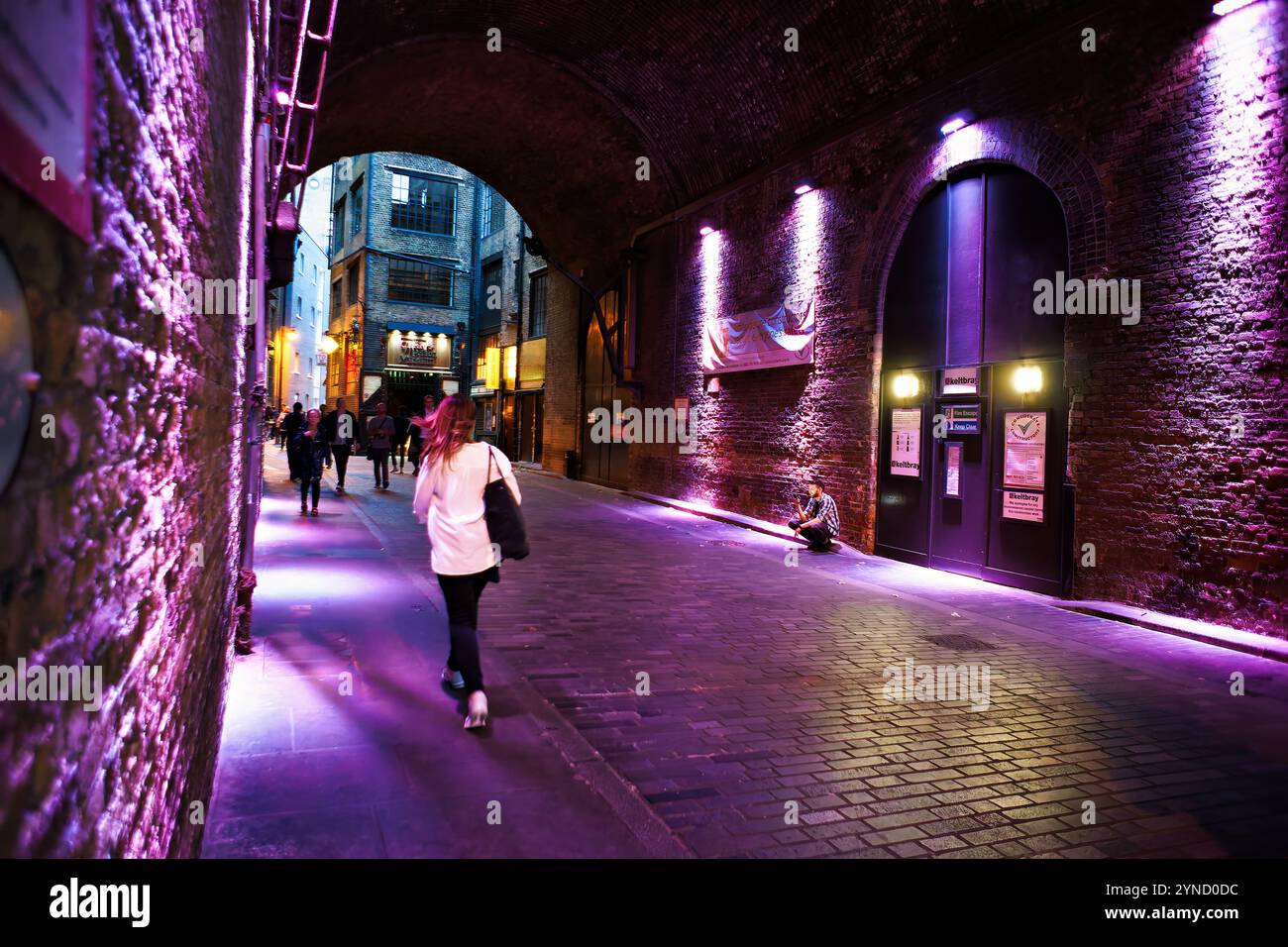 Waterloo Bridge Pedestrian Passage Purple Lighting Londra Inghilterra // LONDRA, Inghilterra - un passaggio pedonale illuminato sotto Waterloo Bridge crea uno spazio urbano distintivo attraverso una spettacolare illuminazione viola. Situato a Lambeth, lungo la South Bank, questo sottopassaggio trasforma una funzionale passerella in uno spazio pubblico dall'atmosfera suggestiva. L'installazione dimostra un uso creativo dell'illuminazione per migliorare le infrastrutture urbane. Foto Stock