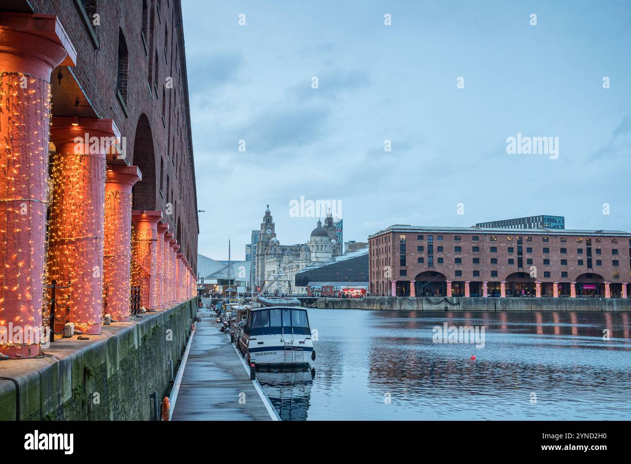 Le luci festive fiancheggiano il Royal Albert Dock che conduce verso le tre Grazie che occupano sullo sfondo del lungomare di Liverpool, nella foto di Mers Foto Stock