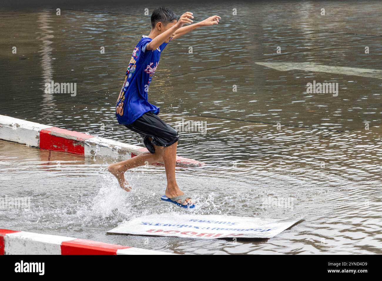 SAMUT PRAKAN, TAILANDIA, 25 2024 settembre, Un ragazzo naviga su un cartellone su una pozzanghera in città Foto Stock