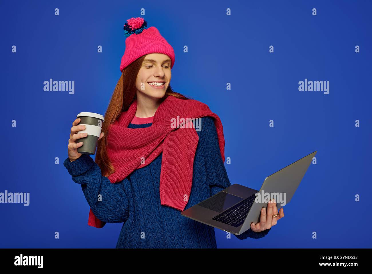 Un giovane emotivo con lunghi capelli rossi si diverte a bere il caffè mentre si impegna con il suo notebook. Foto Stock