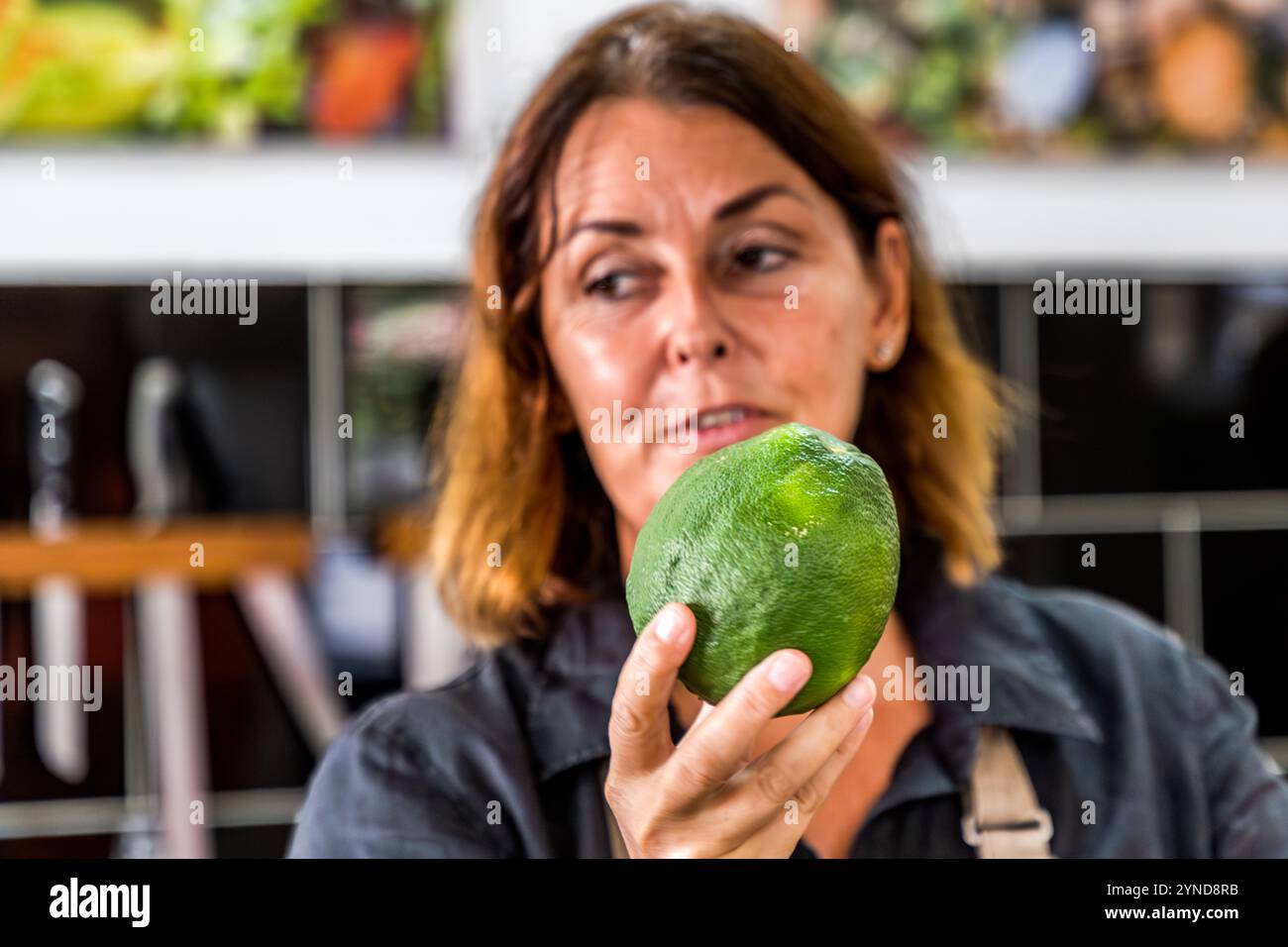 Helmi Smeulders tiene una arancia Laraha (Citrus × aurantium) nella sua scuola di cucina in Djonora Marthaweg, Willemstad, Curaçao. Questa varietà di arancia amara, nativa dell'isola, fornisce la buccia essiccata che conferisce al liquore Original Curaçao di Senior & Co. il suo sapore caratteristico. Foto Stock