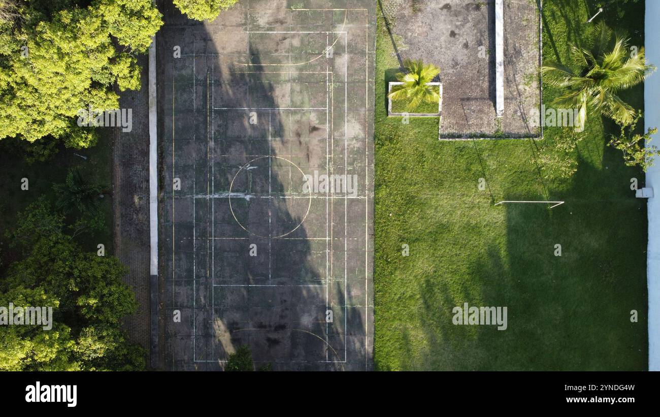 Foto aerea dall'alto verso il basso di un campo multisportivo degradato dal tempo in una piazza alberata e erbosa Foto Stock