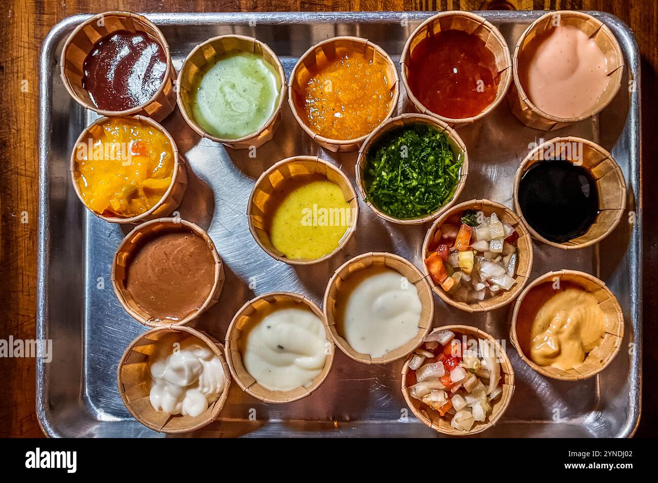 Quattordici salse ispirate ai Caraibi sono disposte su un vassoio al Pasawá Box Eatery di Willemstad, Curaçao – tra cui varietà di mango, chimichurri, senape, noce di cocco e pepe. Questo locale di street food, ospitato in container di spedizione riconvertiti su Caracasbaaiweg, offre una selezione di piatti di varie cucine caraibiche e latinoamericane in modalità self-service. Foto Stock