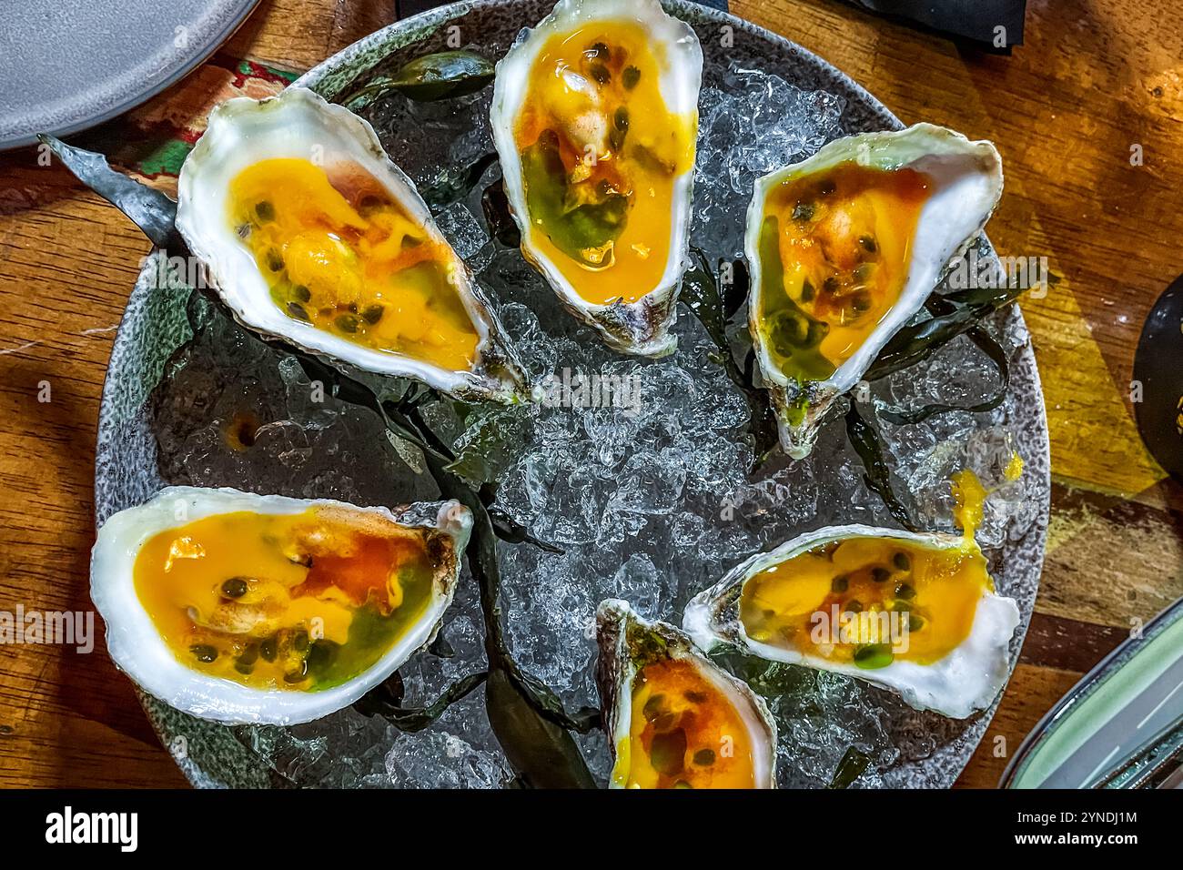 Le ostriche con mango, frutto della passione, coriandolo e peperoncino sono posate su ghiaccio tritato al MosaCaña Bar & Kitchen, Penstraat 41, Willemstad, Curaçao. Il ristorante combina cucina caraibica e latino-americana in un concetto di shared dining, concentrandosi su frutti di mare di provenienza locale e prodotti freschi. Foto Stock