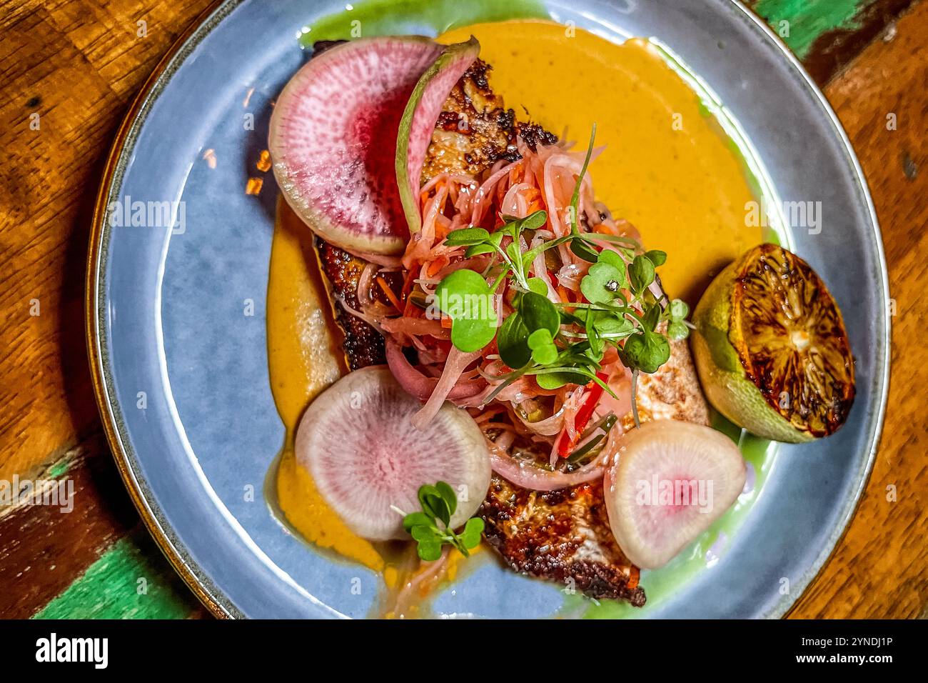 La pesca del giorno, 'Pescado a la Plancha', è servita in curry giallo con daikon e insalata di carote, anguria e ravanello al MosaCaña Bar & Kitchen, Penstraat 41, Willemstad, Curaçao. La cucina prepara pesce pescato fresco quotidianamente nelle acque caraibiche, servito con salse e contorni ispirati all'Asia. Foto Stock