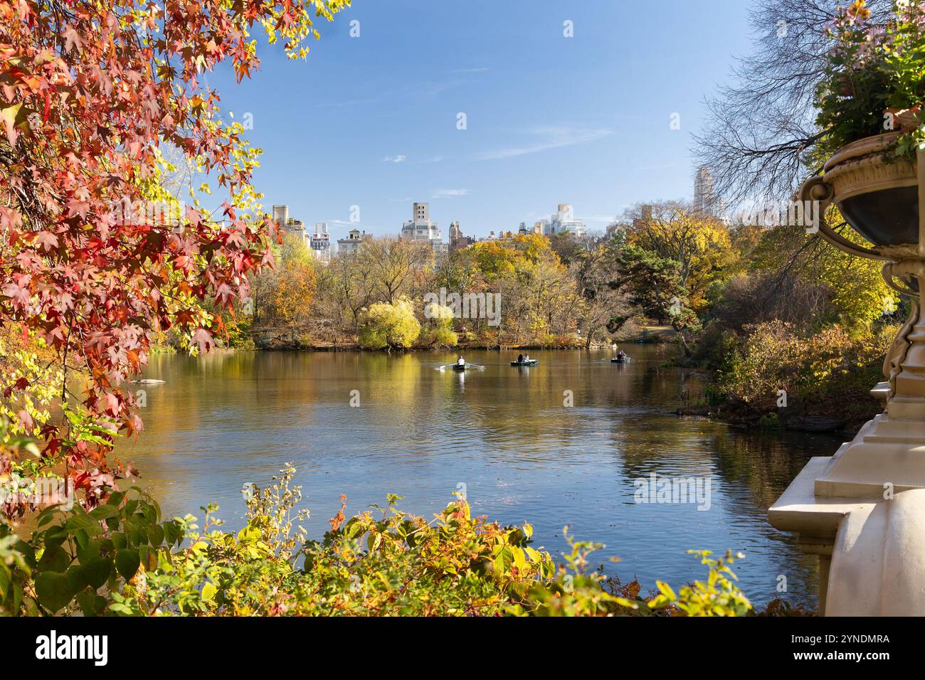 Il vivace fogliame autunnale incornicia un lago tranquillo dove le persone amano andare in barca a remi. I grattacieli si innalzano sullo sfondo sotto un cielo azzurro. Foto Stock
