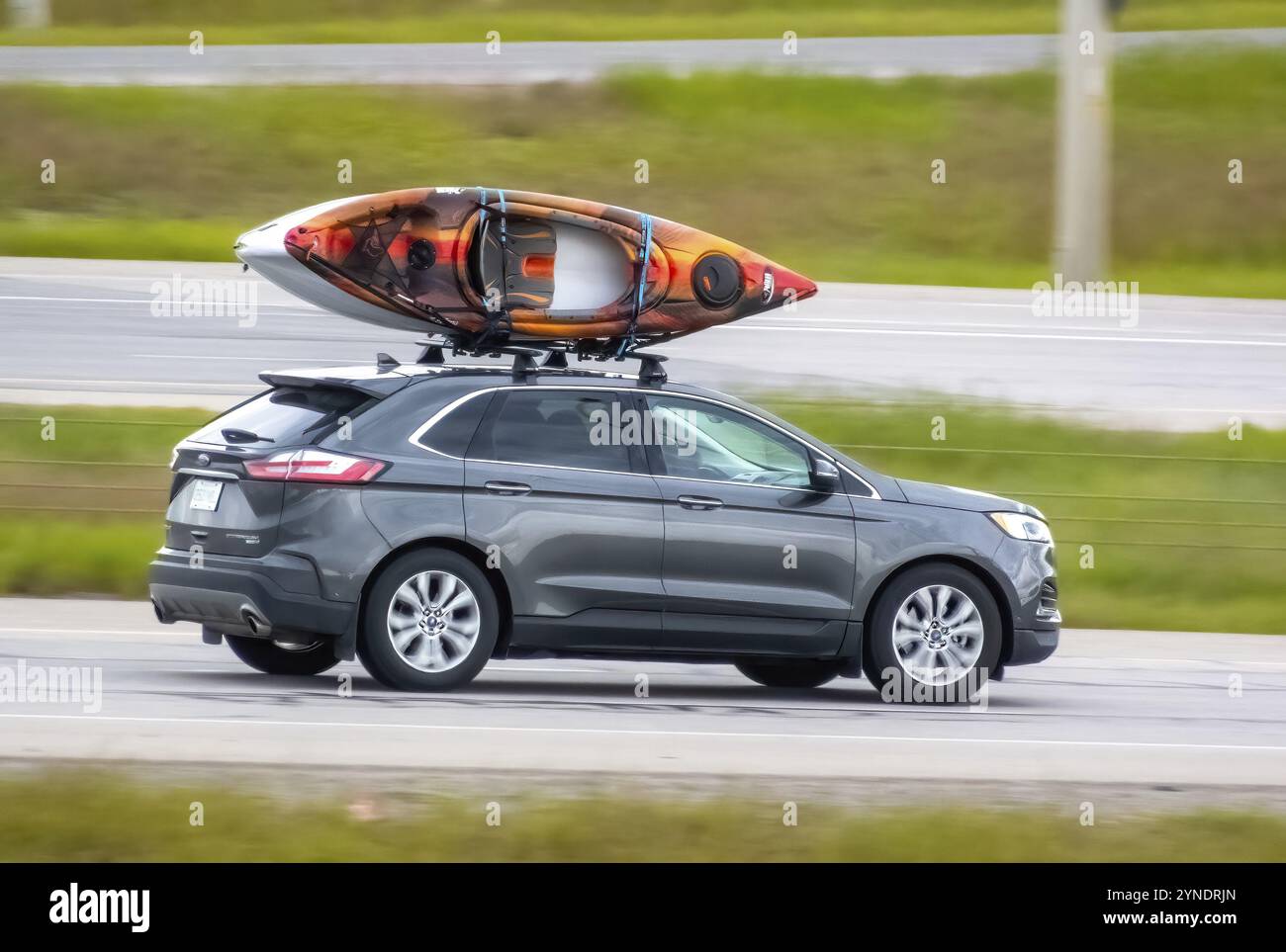 Calgary, Alberta, Canada. 21 giugno 2024. Una Ford Edge grigia percorre un'autostrada con un kayak bianco e arancione fissato montato sul portapacchi nero Foto Stock