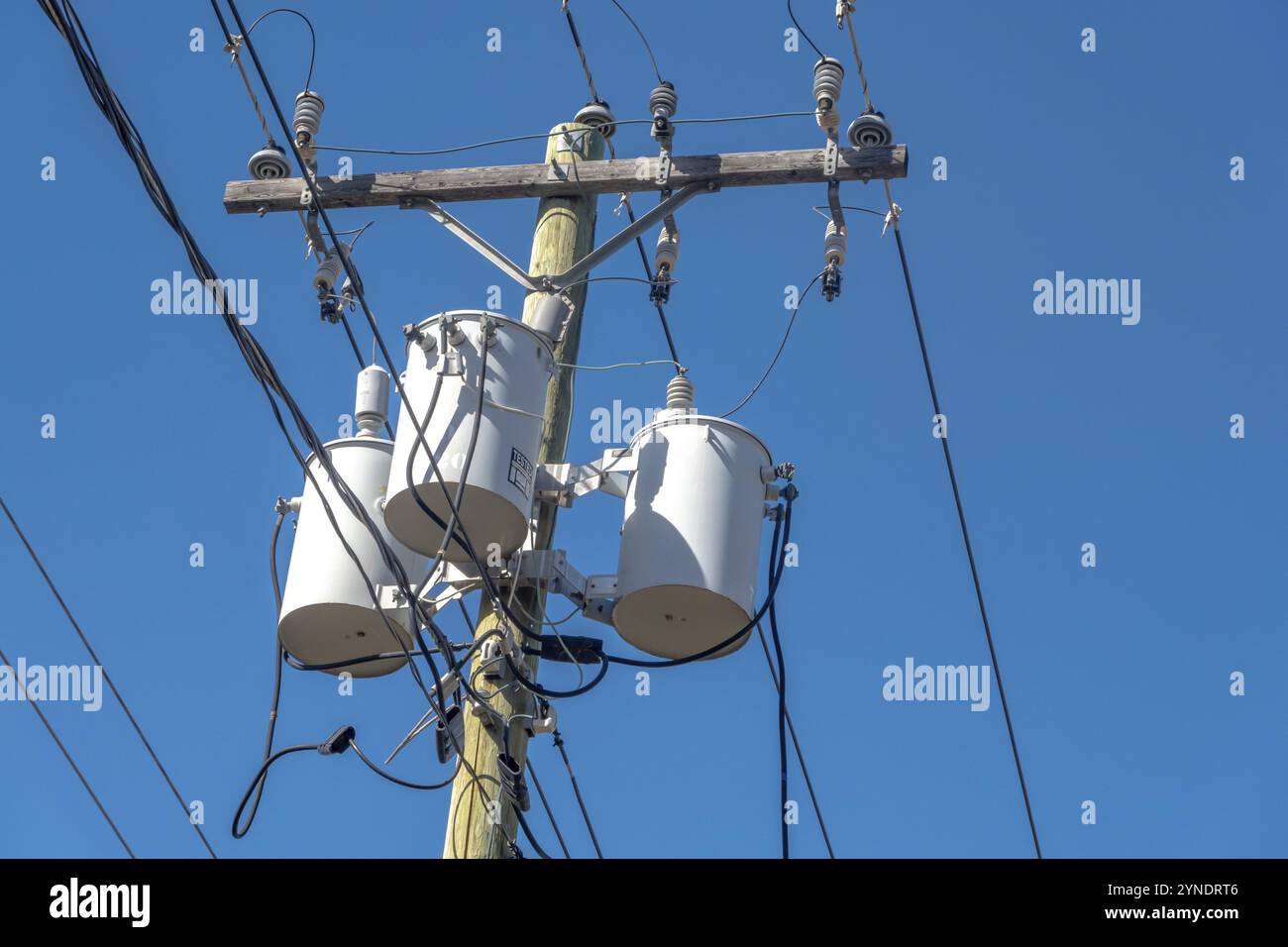 Calgary, Alberta, Canada. 7 aprile 2023. Banco di trasformatori ad asta con tre trasformatori di distribuzione bianchi su palo con cielo blu Foto Stock