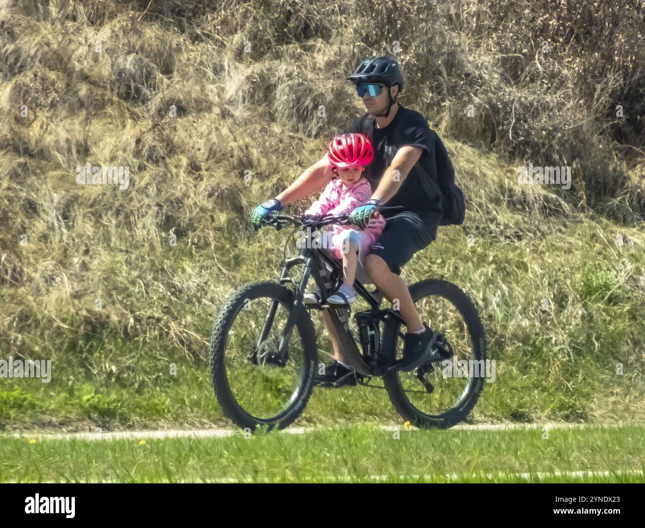 Calgary, Alberta, Canada. 10 maggio 2024. Una persona in bicicletta con un bambino in primavera Foto Stock