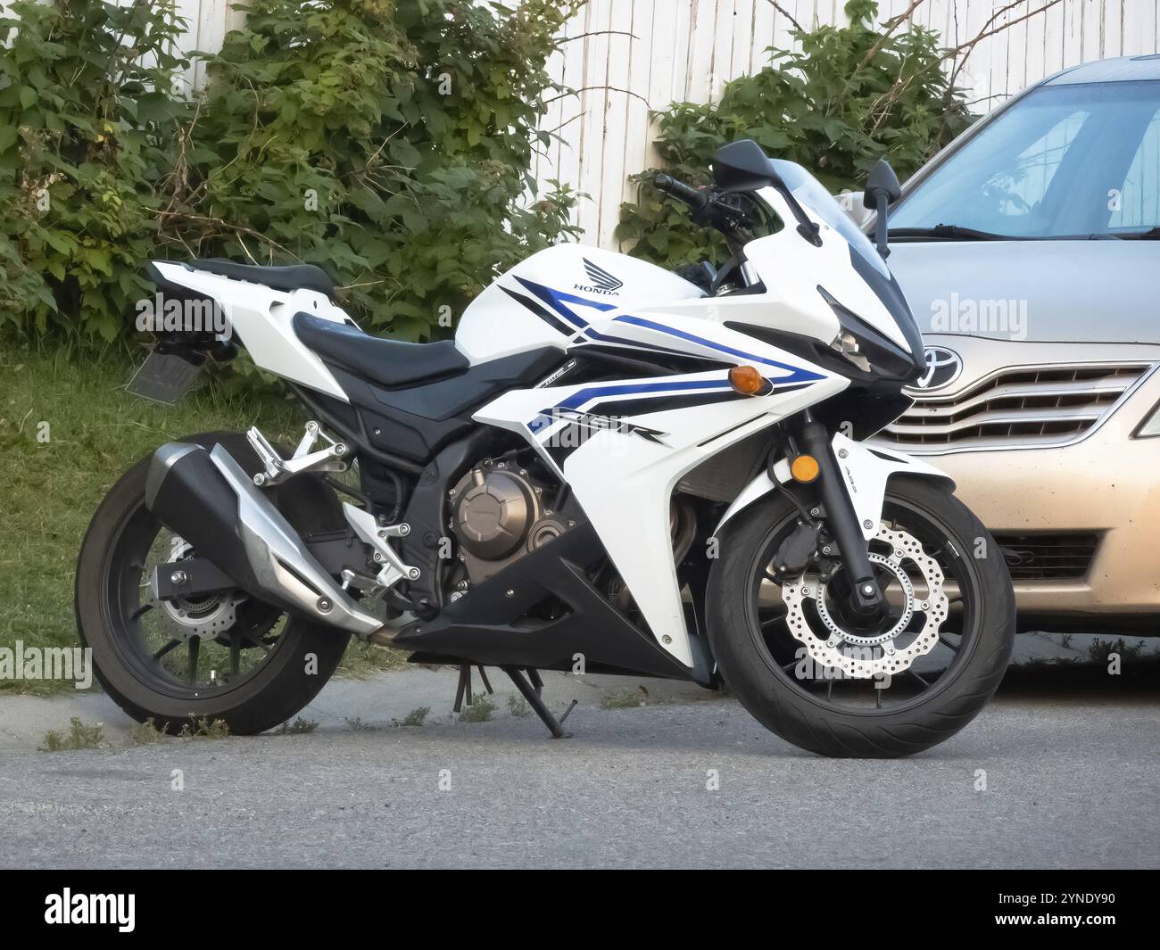 Calgary, Alberta, Canada. 21 luglio 2024. Un'elegante moto bianca Honda CBR500R parcheggiata accanto a un'auto Foto Stock