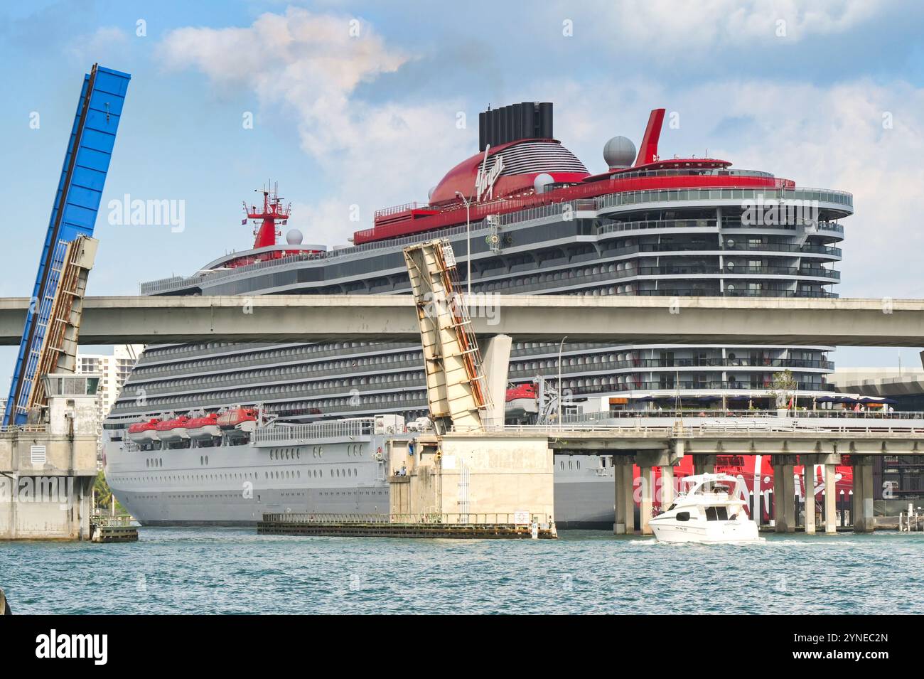 Miami, Florida, Stati Uniti - 3 dicembre 2023: Il peschereccio sta per passare il ponte sopraelevato all'ingresso del porto. Sullo sfondo c'è una nave da crociera Virgin Foto Stock