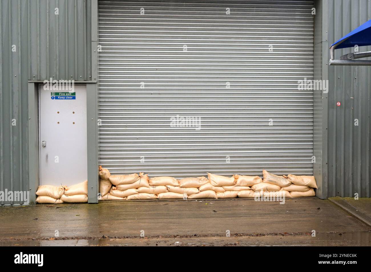 Sacchetti di sabbia impilati contro la porta a rulli di una fabbrica per evitare inondazioni dovute all'acqua inondabile in seguito a forti piogge provocate da una tempesta Foto Stock