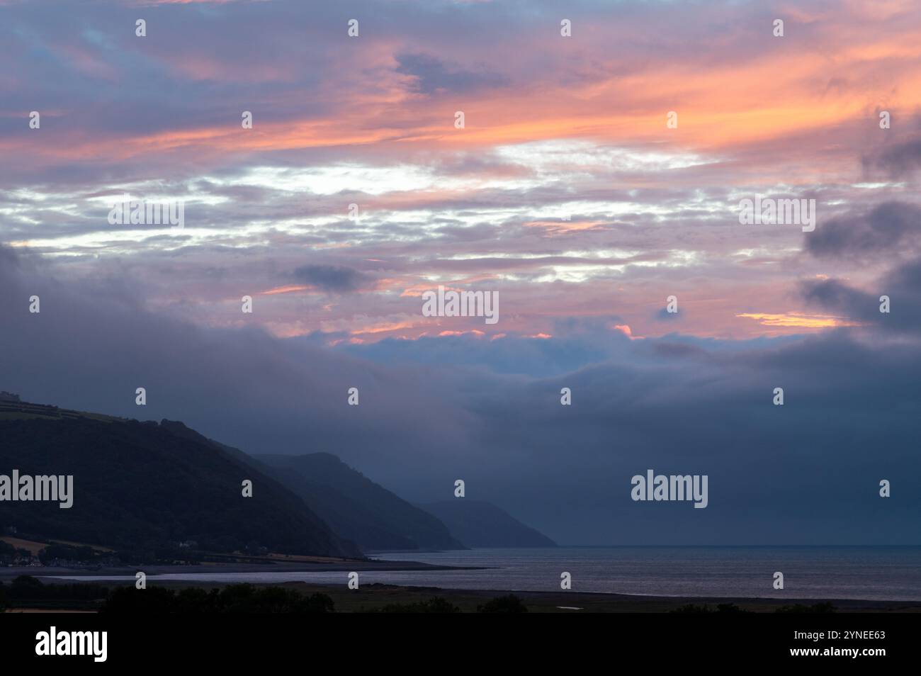 Un tramonto basso, piovoso e nuvoloso sulla baia di Porlock con il promontorio di Gore Point che scende verso il mare Foto Stock