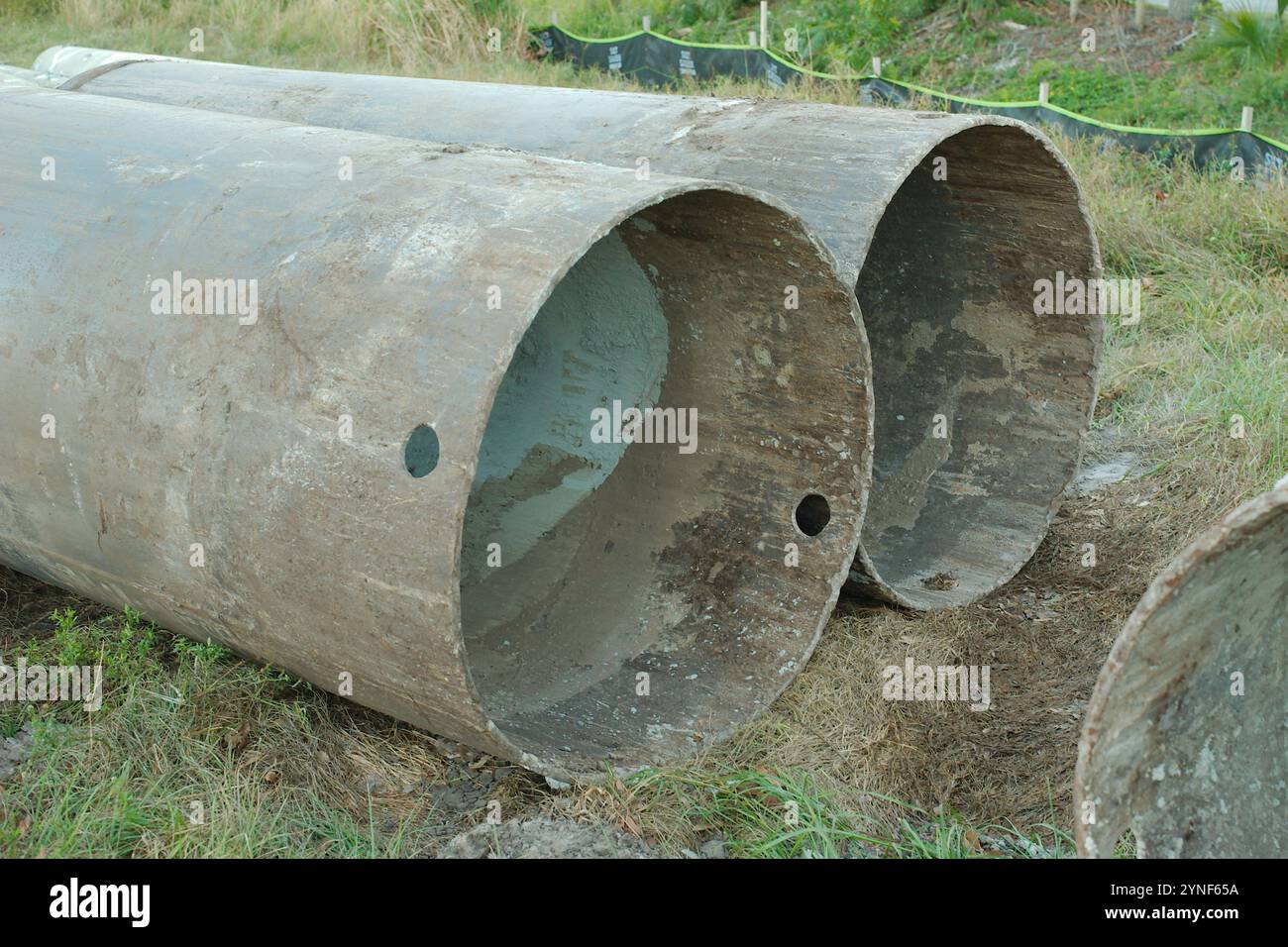 Due grandi tubi metallici arrugginiti utilizzati nelle fondazioni edili costruzione di pali elettrici in un campo. Silt fence in background. Foto Stock