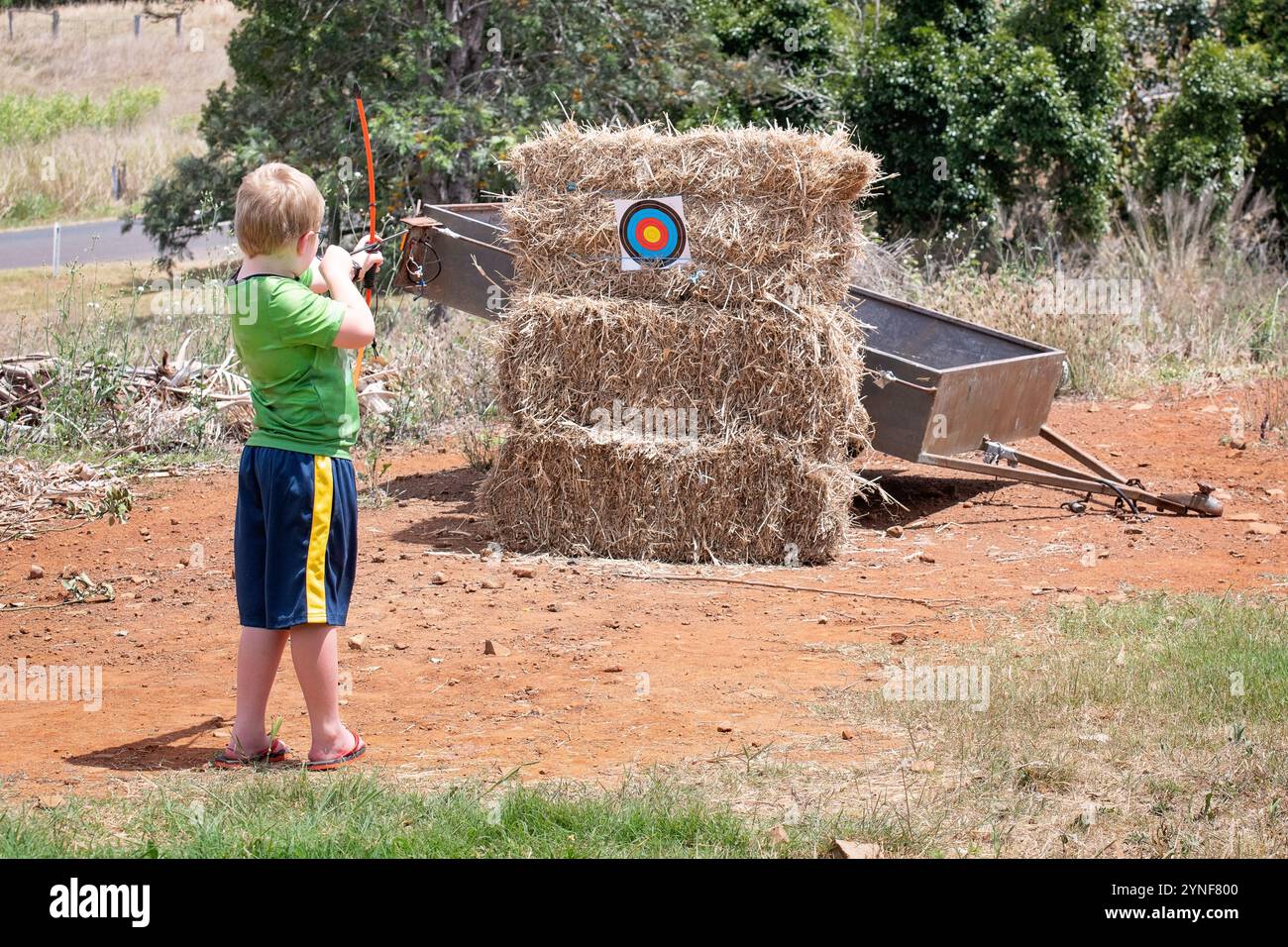 ragazzo che spara arco e freccia al bersaglio su balle di fieno, area rurale per bambini Foto Stock