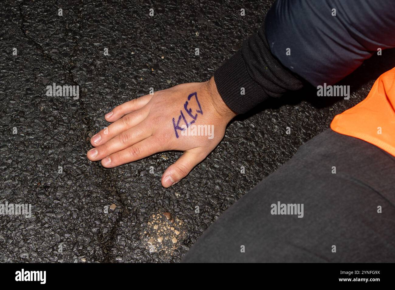 Una mano attivista a terra con la colla scritta sopra durante la manifestazione. (Ostatnie Pokolenie/Last Generation) ha avviato una serie di blocchi su Wislostrada per sfidare le politiche climatiche del governo sotto Donald Tusk. Intorno alle 7:00, una dozzina di attivisti con gilet arancioni bloccarono il traffico vicino all'ingresso del tunnel. Portavano striscioni, tra cui uno che diceva: "Tusk Fuels Climate Collapse". Il gruppo ha annunciato piani per tornare settimanalmente, con l'obiettivo di stabilire Wislostrada come simbolo di resistenza civile sostenuta. Foto Stock