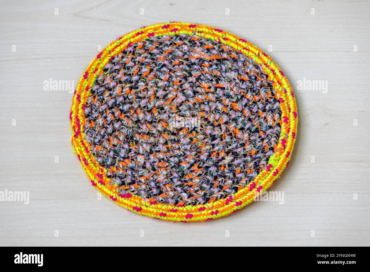 Pattino da tavolo rotondo colorato fatto a mano su sfondo in legno. Tappetino in tessuto lavorato a mano per arredare la casa. Foto Stock