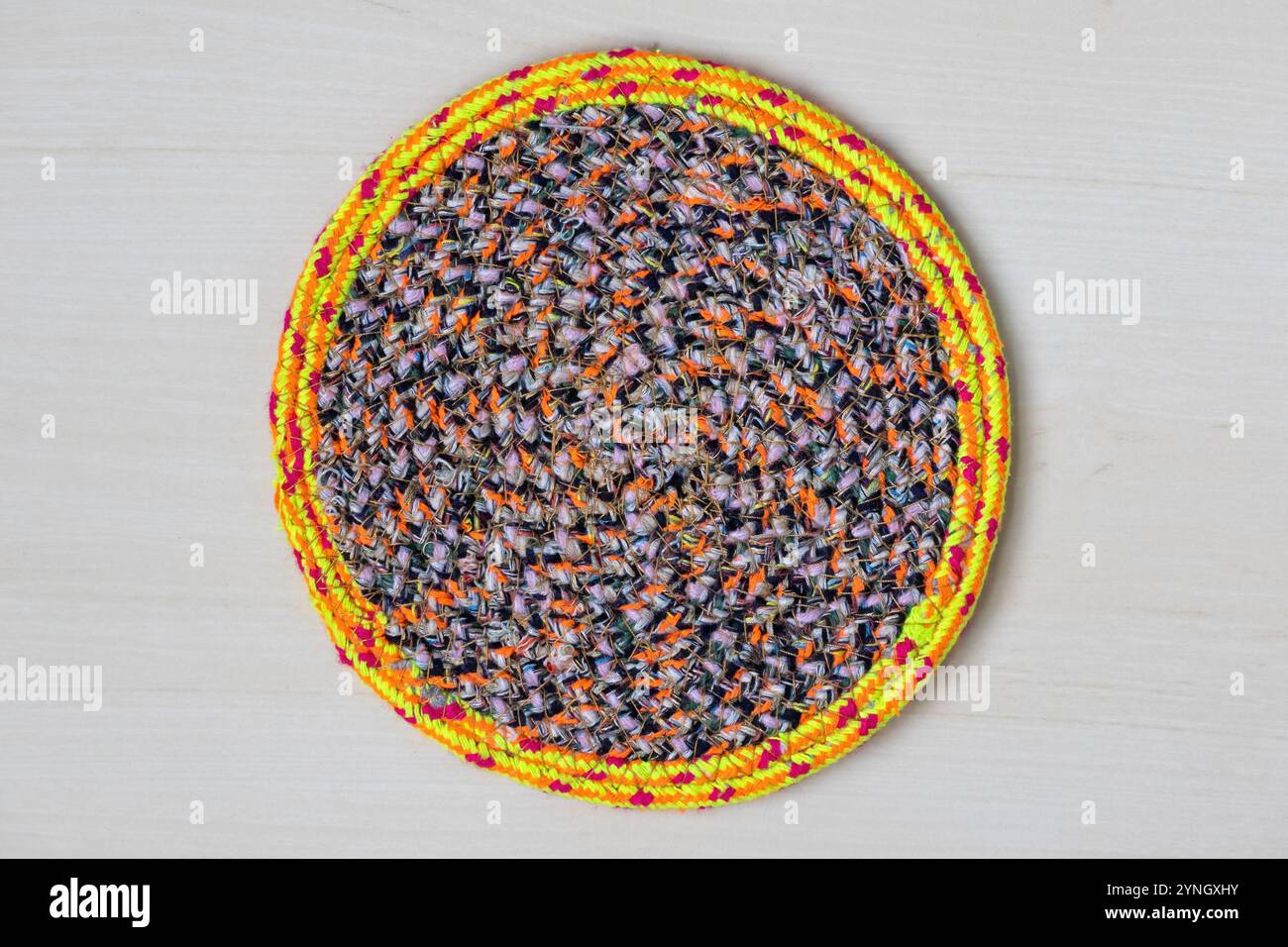 Pattino da tavolo rotondo colorato fatto a mano esposto su uno sfondo di legno. Vista dall'alto del tappetino in tessuto lavorato a mano, perfetto per le decorazioni domestiche. Foto Stock