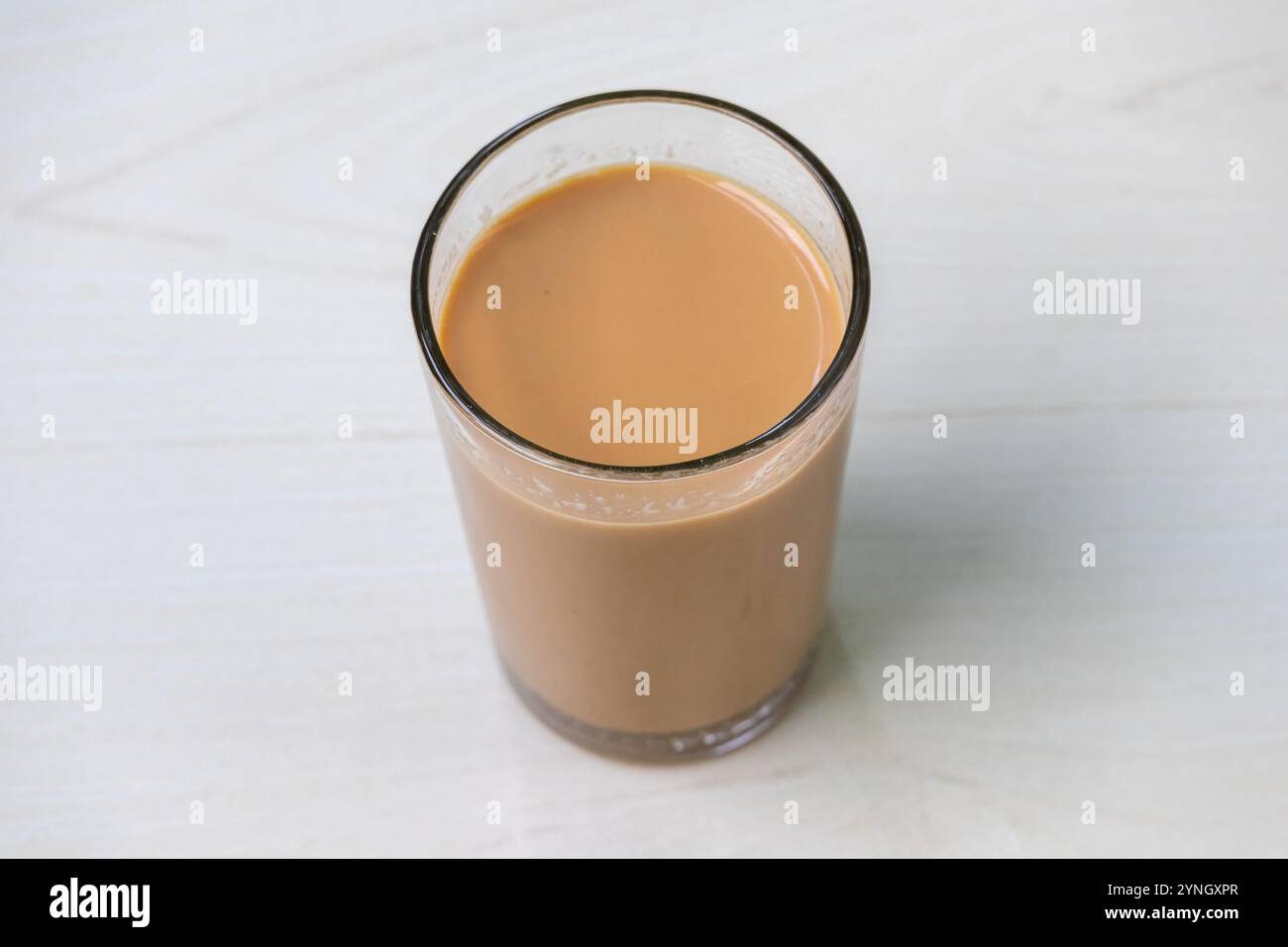 Un bicchiere di tè al latte caldo (dudh cha) su una superficie di legno chiaro. Foto Stock