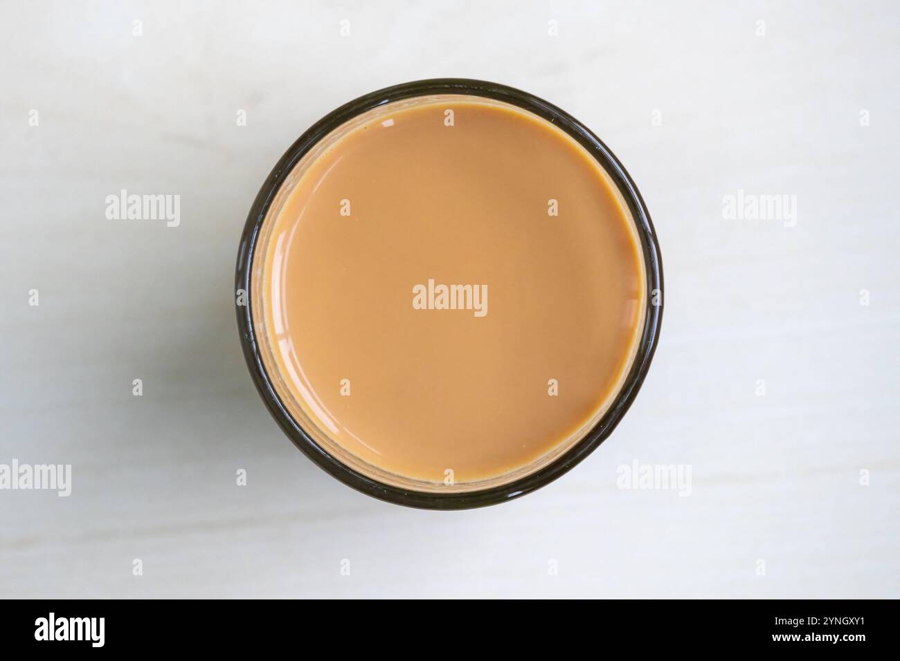 Tè al latte caldo o dudh cha in una tazza di vetro, tenuto su una superficie di legno chiaro. Vista dall'alto. Foto Stock
