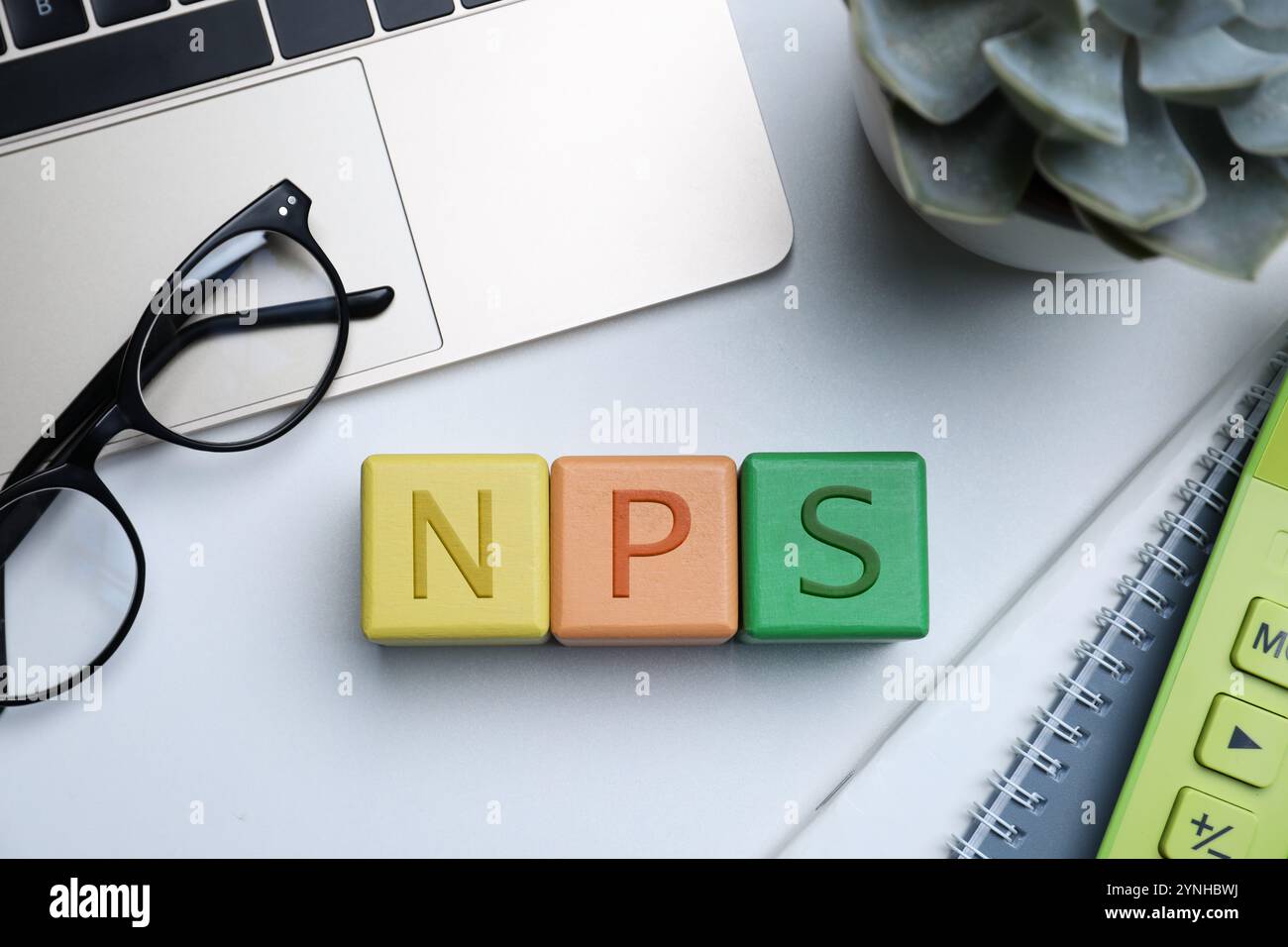 NPS (NET promoter score) abbreviazione composta da cubi, laptop e cancelleria su tavolo grigio, piatto Foto Stock