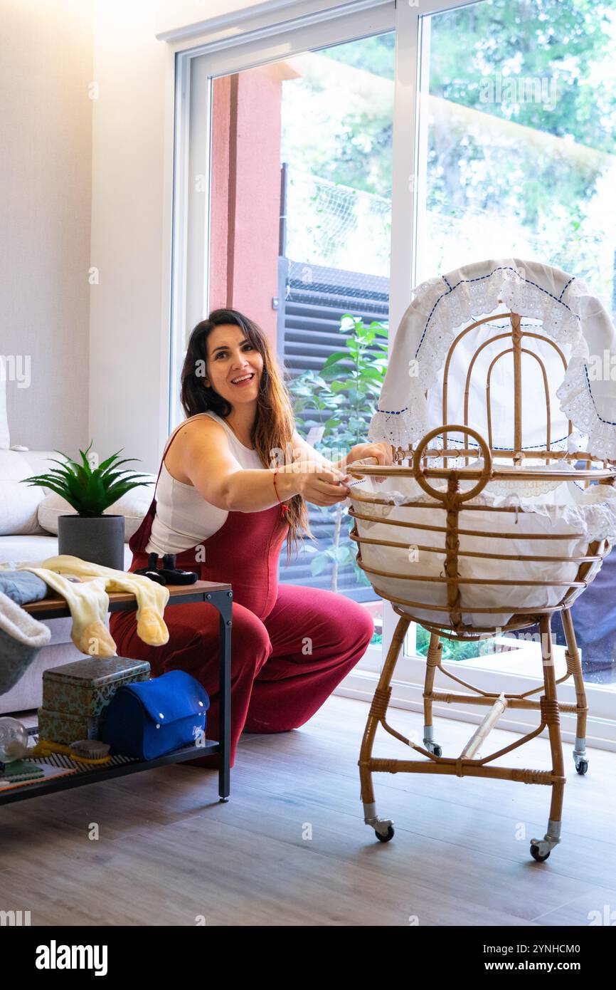 Donna incinta sorridente che prepara la culla del futuro bambino a casa Foto Stock