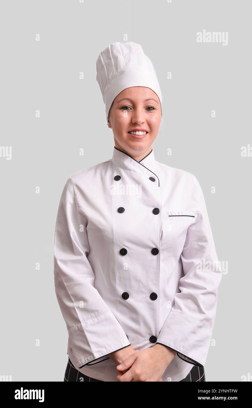 Chef donna sicura che sorride indossando una divisa bianca e un cappello da chef, che rappresentano l'esperienza culinaria e la professionalità Foto Stock