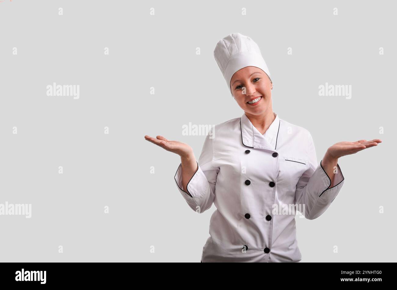Una cuoca felice che presenta qualcosa con le mani, indossa uniforme bianca e cappello da chef Foto Stock
