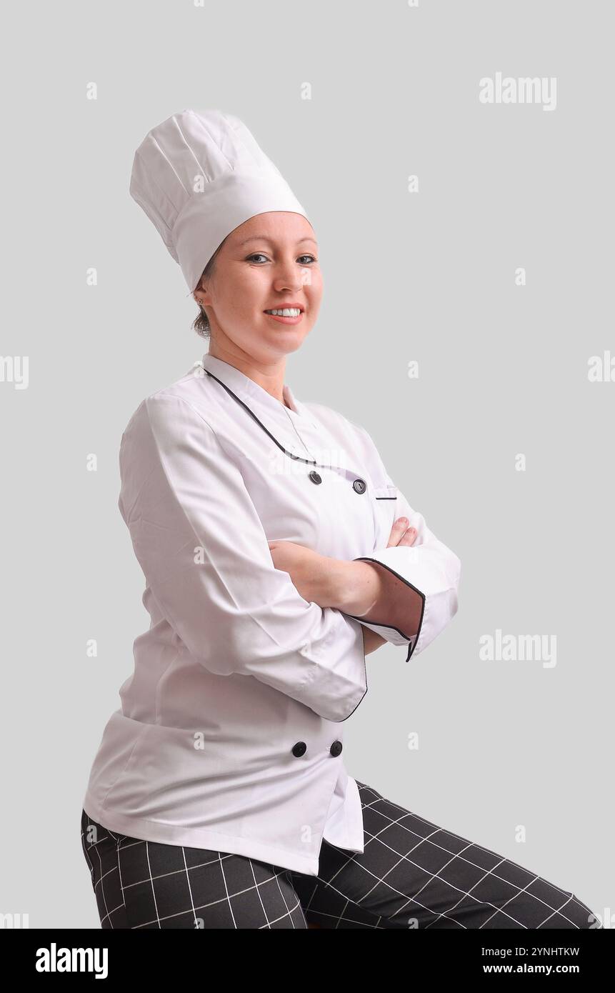 Chef donna sicura in uniforme sorridente e in posa con le braccia incrociate, incarnando professionalità ed esperienza culinaria Foto Stock